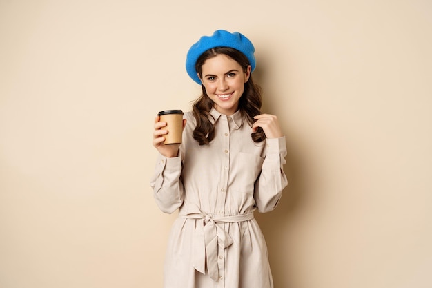 Hermosa chica moderna posando con una taza de café para llevar bebiendo de una taza reutilizable de café y pos...