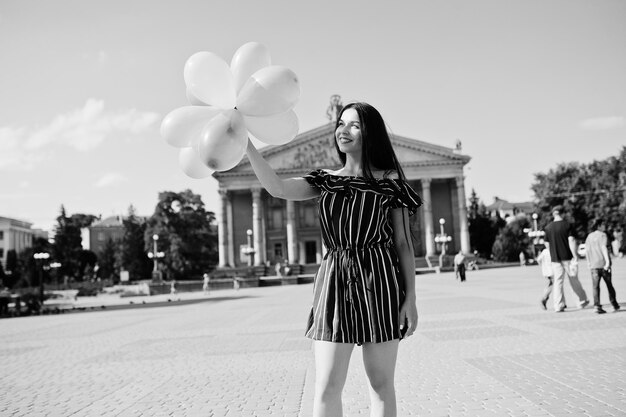 Hermosa chica morena en la calle de la ciudad con globos en las manos