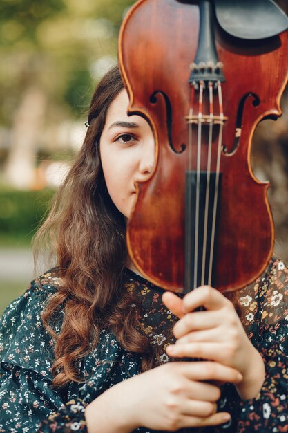 Hermosa chica en un parque de verano con un violín