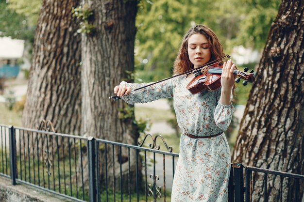 Hermosa chica en un parque de verano con un violín