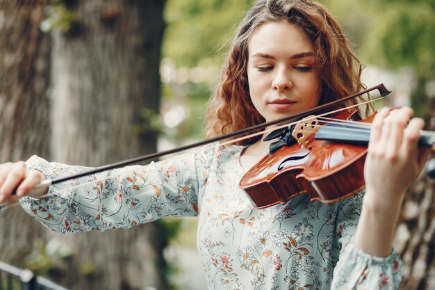 Hermosa chica en un parque de verano con un violín