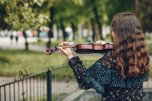 Hermosa chica en un parque de verano con un violín