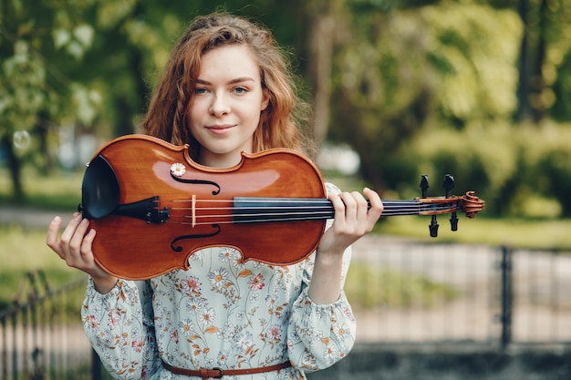 Hermosa chica en un parque de verano con un violín