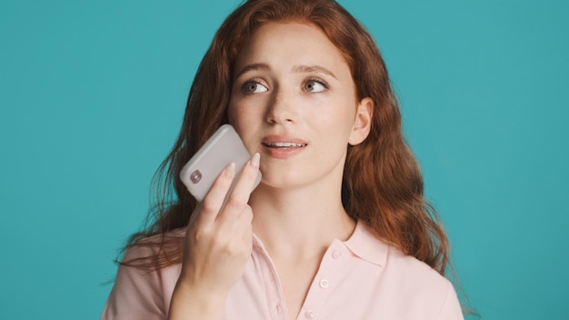 Hermosa chica pelirroja grabando un mensaje de voz en un smartphone sobre un fondo colorido