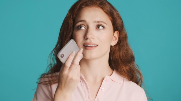 Hermosa chica pelirroja grabando un mensaje de voz en un smartphone sobre un fondo colorido