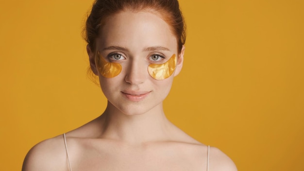 Foto gratuita hermosa chica pelirroja con parches dorados en los ojos mirando con confianza a la cámara sobre un fondo colorido