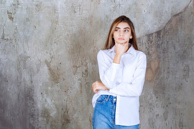 Hermosa chica de pelo largo en blusa blanca pensando en algo