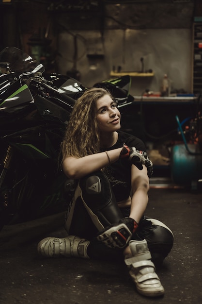 Hermosa chica con el pelo largo en el garaje reparando una motocicleta.