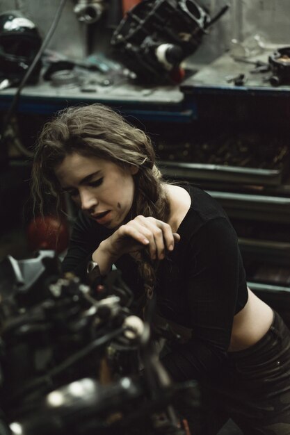 Hermosa chica con el pelo largo en el garaje reparando una motocicleta.