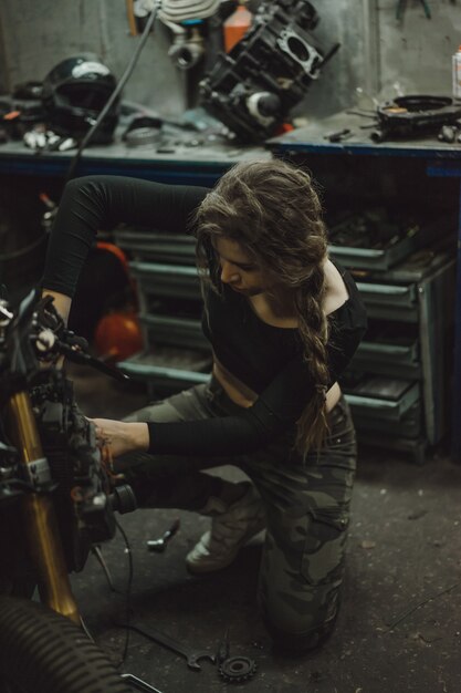 Hermosa chica con el pelo largo en el garaje reparando una motocicleta.