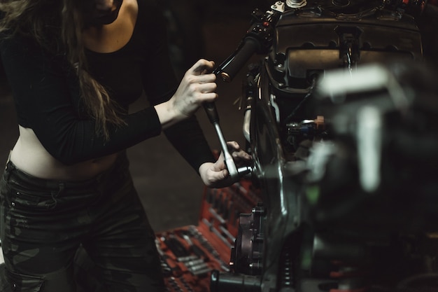 Hermosa chica con el pelo largo en el garaje reparando una motocicleta.