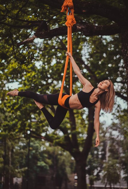 Hermosa chica pensativa con cabello largo está haciendo ejercicios en cabestrillo en el bosque de verano.