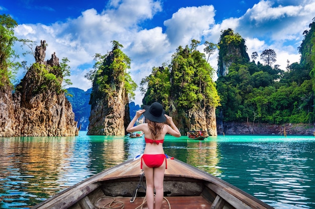 Hermosa chica de pie en el barco y mirando a las montañas en la presa Ratchaprapha en el Parque Nacional Khao Sok, provincia de Surat Thani, Tailandia.