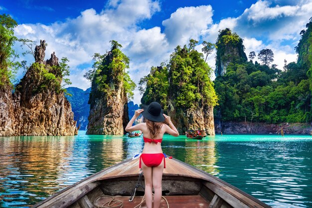 Hermosa chica de pie en el barco y mirando a las montañas en la presa Ratchaprapha en el Parque Nacional Khao Sok, provincia de Surat Thani, Tailandia.