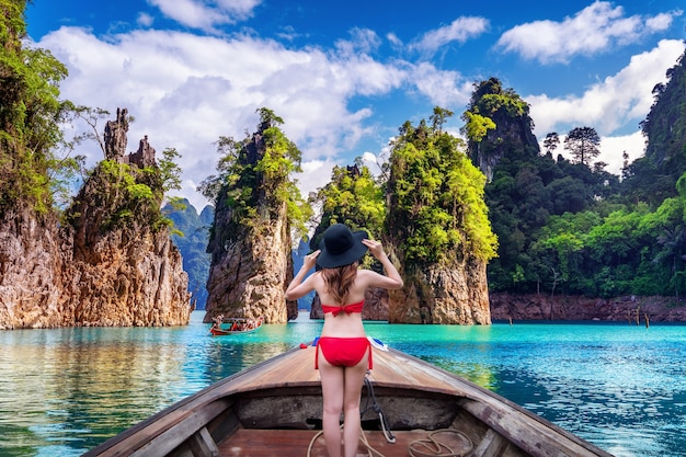 Hermosa chica de pie en el barco y mirando a las montañas en la presa Ratchaprapha en el Parque Nacional Khao Sok, provincia de Surat Thani, Tailandia.