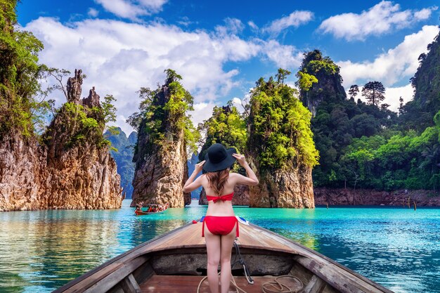 Hermosa chica de pie en el barco y mirando a las montañas en la presa Ratchaprapha en el Parque Nacional Khao Sok, provincia de Surat Thani, Tailandia.