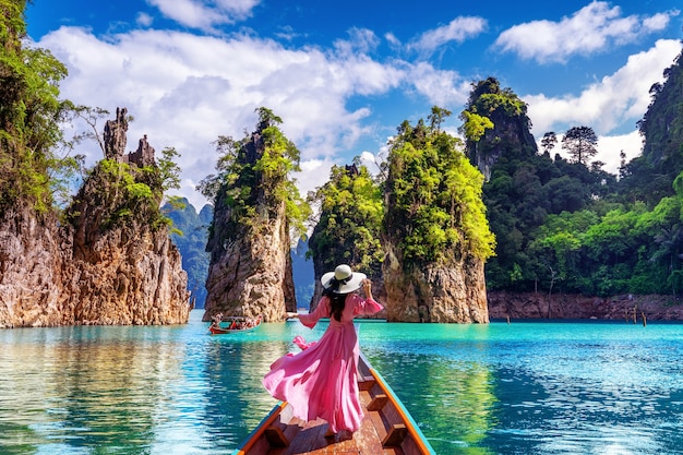 Hermosa chica de pie en el barco y mirando a las montañas en la presa Ratchaprapha en el Parque Nacional Khao Sok, provincia de Surat Thani, Tailandia.