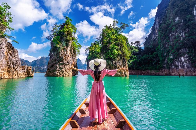 Hermosa chica de pie en el barco y mirando a las montañas en la presa Ratchaprapha en el Parque Nacional Khao Sok, provincia de Surat Thani, Tailandia.