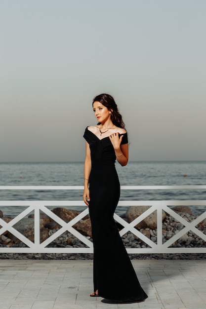 Foto gratuita hermosa chica de pie cerca de la playa en vestido largo negro durante el día