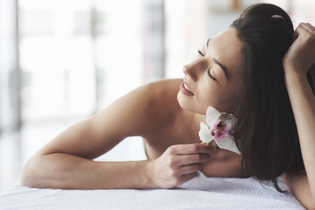 Hermosa chica con una piel perfecta de orquídea cerca de la ventana grande.