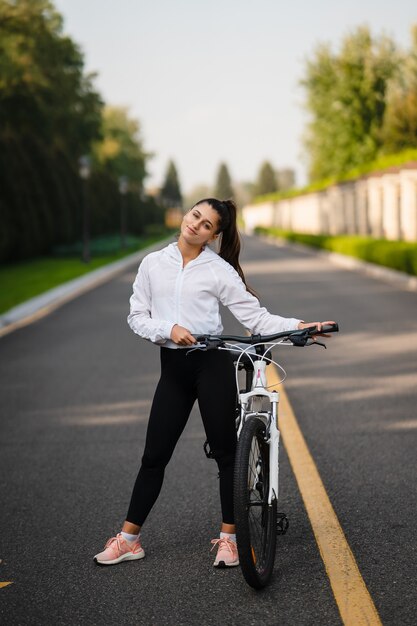 Hermosa chica posando en bicicleta blanca. Camina en la naturaleza.