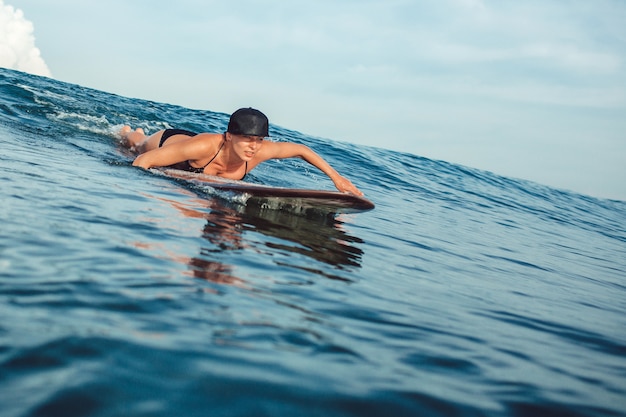 Hermosa chica posando sentado en una tabla de surf en el océano