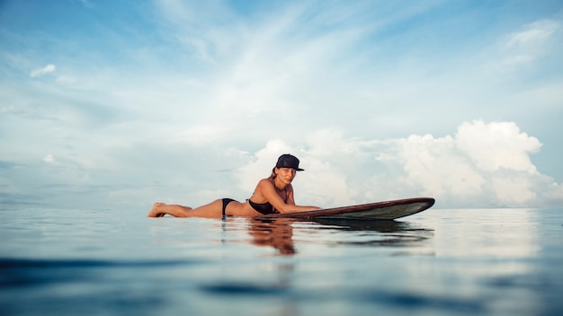 Hermosa chica posando sentado en una tabla de surf en el océano