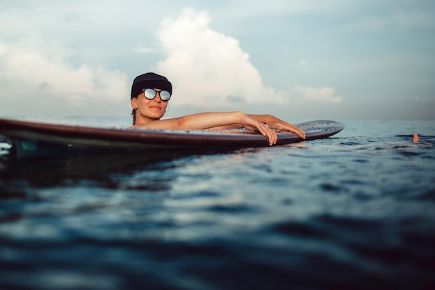 Hermosa chica posando sentado en una tabla de surf en el océano