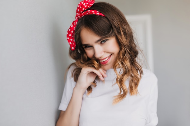 Hermosa chica positiva expresando buenas emociones. Mujer atractiva rizada con cinta roja sonriendo.