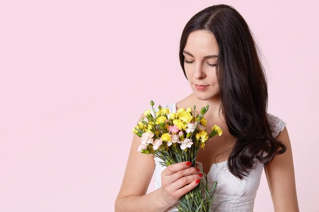 Hermosa chica con ramo de flores aisladas en rosa, morena mujer mirando hacia abajo en su presente