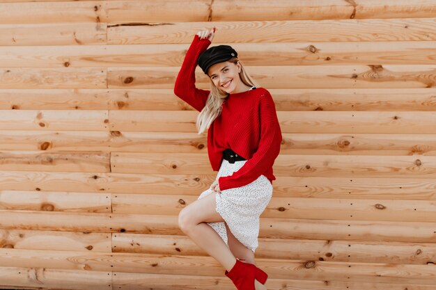 Hermosa chica rubia está loca y divertida en la pared de madera. Hermosa mujer en vestido blanco de moda pasar un buen rato al aire libre.