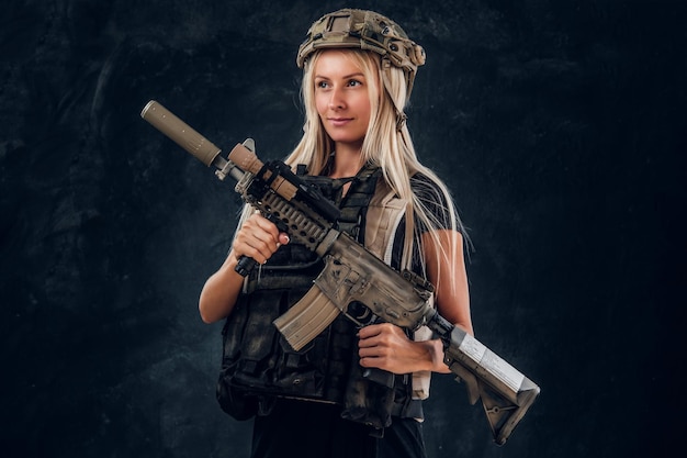 Hermosa chica rubia frágil con ametralladora en uniforme militar completo y casco.