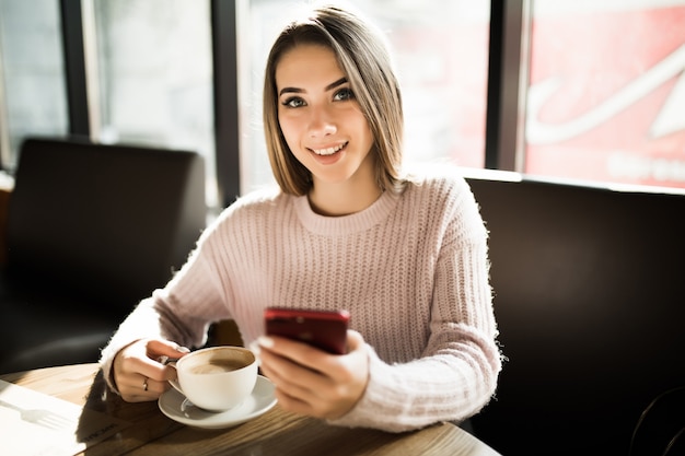 Hermosa chica rubia usando su teléfono móvil en la cafetería durante el almuerzo de café a la hora del día