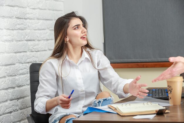 Una hermosa chica sentada detrás del escritorio y hablando con alguien.