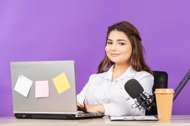 Hermosa chica sentada detrás del escritorio y sonriendo a la cámara Foto de alta calidad