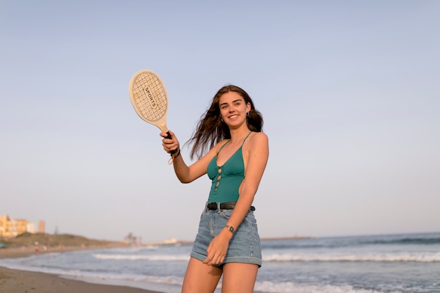 Hermosa chica sentada en la orilla del mar jugando raqueta