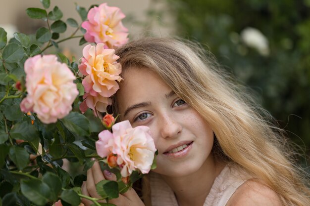 Hermosa chica sentada y sonriendo cerca de las flores, afuera durante el día.