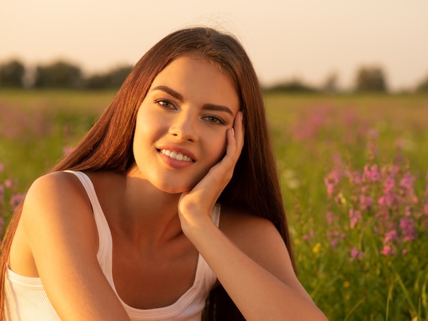 Hermosa chica sexy está en la naturaleza en el fondo de flores silvestres de primavera.