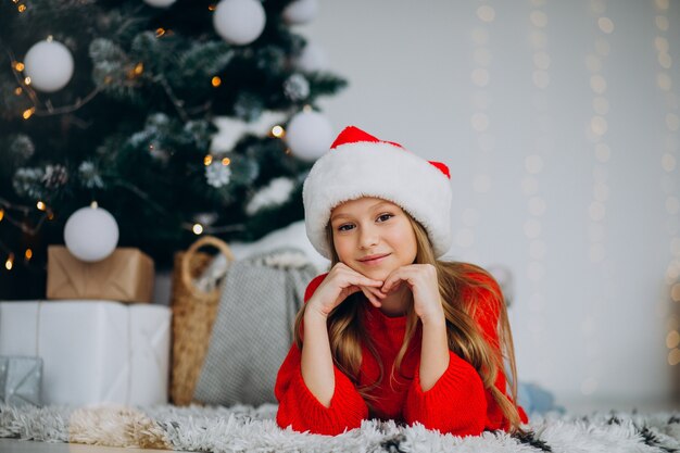 Hermosa chica con sombrero de santa bajo el árbol de Navidad