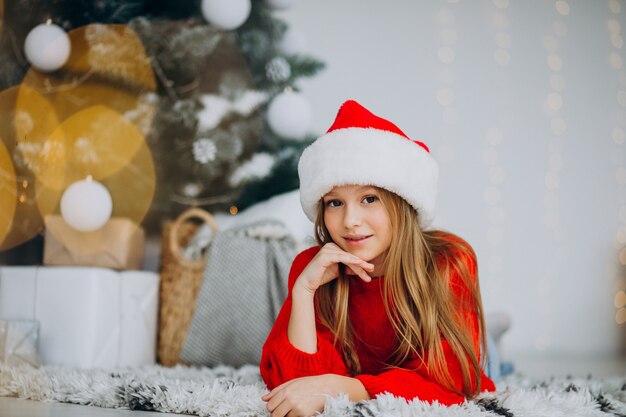 Hermosa chica con sombrero de santa bajo el árbol de Navidad