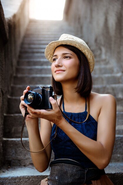 Hermosa chica con sombrero sonriendo, tomando fotos, sentado en las escaleras.