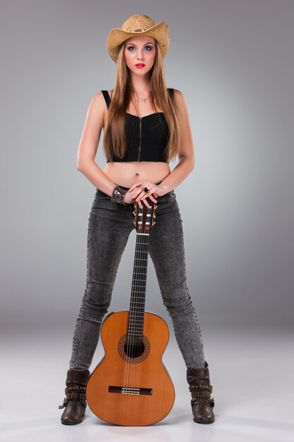 Hermosa chica en un sombrero de vaquero y guitarra acústica.