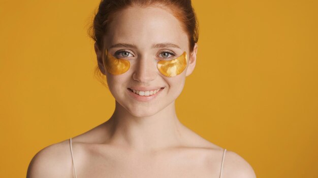 Hermosa chica sonriente con parches dorados en los ojos mirando felizmente a la cámara sobre un fondo colorido