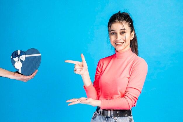 Hermosa chica sonriente señalando con el dedo el cuadro actual en el fondo azul