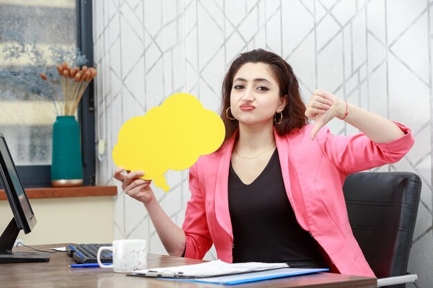 Hermosa chica sosteniendo una burbuja de idea amarilla en forma de nube y gestos con el pulgar hacia abajo Foto de alta calidad