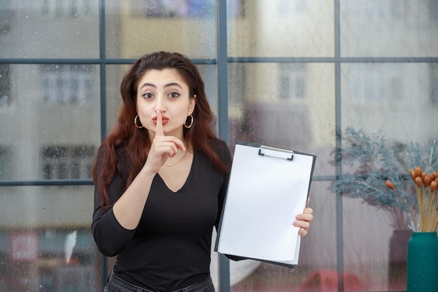 Hermosa chica sosteniendo cuaderno y gesto silencioso Foto de alta calidad