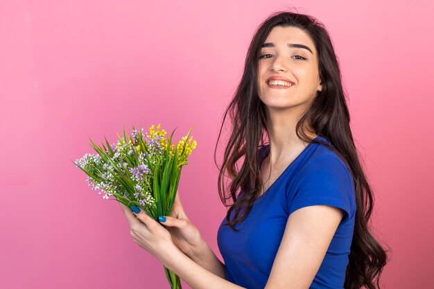 Hermosa chica sosteniendo un ramo de flores y sonriendo a la cámara