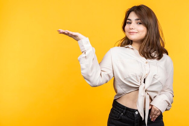 Hermosa chica sosteniendo su mano y sonriendo a la cámara Joven sobre fondo amarillo aislado Foto de alta calidad