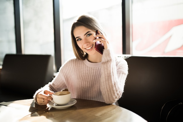 Hermosa chica con su teléfono móvil en la cafetería durante el café después del estudio del trabajo