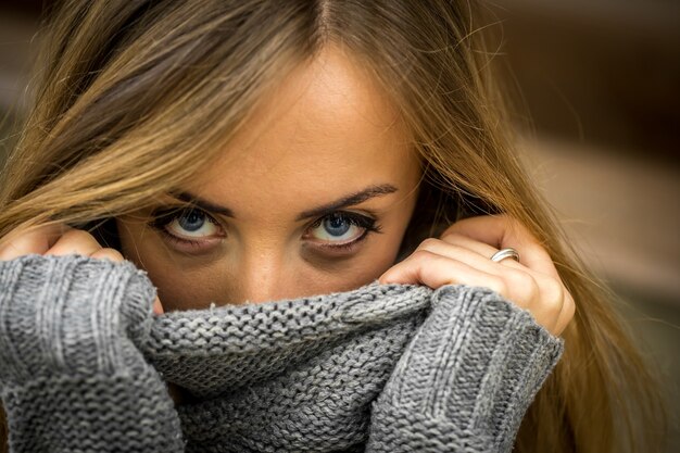 Hermosa chica en un suéter con cabello largo y labios rojos en la pared de troncos de madera